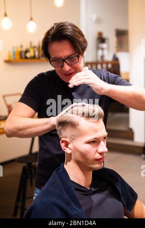 Barber frotte les cheveux d'un jeune homme avec de la pommade dans son salon de coiffure après avoir coupé ses cheveux Banque D'Images