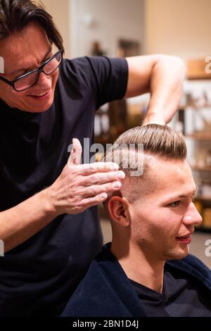 Barber frotte les cheveux d'un jeune homme avec de la pommade dans son salon de coiffure après avoir coupé ses cheveux Banque D'Images