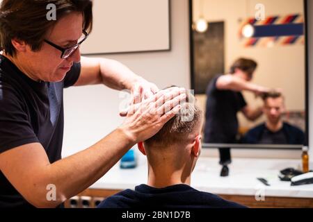 Barber frotte les cheveux d'un jeune homme avec de la pommade dans son salon de coiffure après avoir coupé ses cheveux Banque D'Images