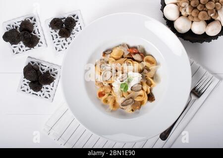 Pâtes d'orecchiette avec ceps, tomates cerises, gratin de ricotta, truffes fraîches et champignons sauvages. L'orecchiette est une pâte typique d'Apulia, une région o Banque D'Images