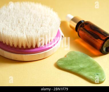 Brosse pour corps sèche, bouteille d'huile et masseur à base de gua sha sur fond jaune. Concept de soins de beauté Banque D'Images