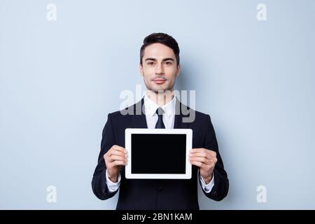 Beau jeune économiste brunete gars avec chaume tient la tablette avec écran noir. Il porte une tenue habillée et une cravate, se tient sur une lumière Banque D'Images