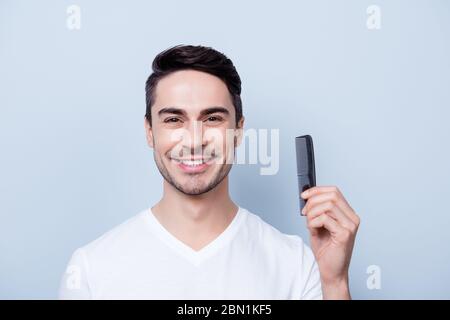 Concept de salon de coiffure. Souriant, le jeune brunete en t-shirt blanc est debout sur le fond pur, tient un peigne dans la main. Sa coiffure est Banque D'Images