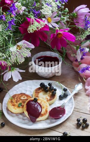 Petit-déjeuner de crêpes, quark, crème de cassis et groseilles un bouquet de fleurs sauvages sur un fond de bois. Banque D'Images