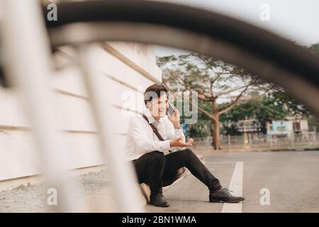 Jeune homme barbu à la mode à l'aide d'une tablette numérique , souriant gaiement, regarder ou lire quelque chose de drôle, assis sur le sol, près de la bicycl Banque D'Images