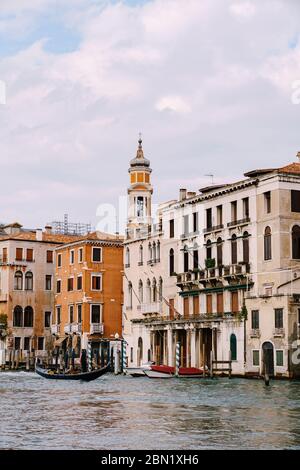Une gondole avec des touristes navigue le long du Grand Canal au milieu des façades de maisons vénitiennes debout sur l'eau à Venise, en Italie. Banque D'Images