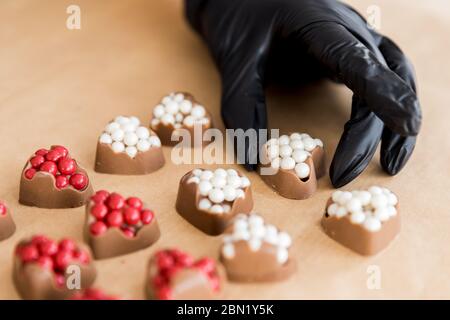 Chocolats gros plan en forme de coeur avec garniture rouge dans les mains de la femme de confiseuse sur fond de cuisine Banque D'Images