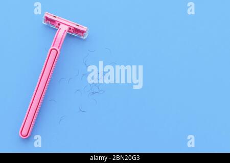 machine à raser pour femmes rose et cheveux sur fond bleu. Le concept du rasage pour femmes. Banque D'Images