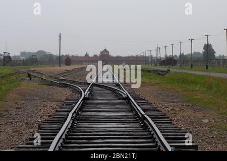 Musée Mémorial de l'Holocauste d'Auschwitz - vue de l'intérieur du camp le long des voies ferrées avec le portier d'Auschwitz II-Birkenau à distance, par une journée de dépassement Banque D'Images