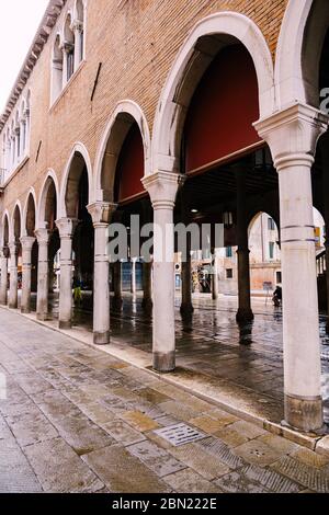 Venise, Italie - 04 octobre 2019 : un bâtiment à Venise, debout sur des colonnes. Mur en pierre de briques brunes, colonnes blanches et arches hautes, pavage ancien Banque D'Images