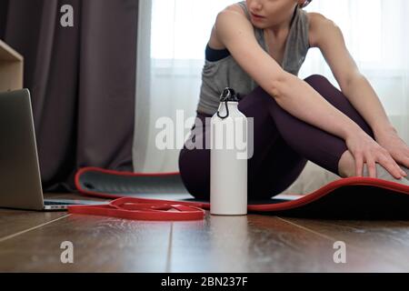 Une fille dans un uniforme de sport est assise sur le sol et regarde dans un ordinateur portable, le foyer sur l'agitateur à côté d'elle. Banque D'Images