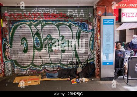 Homme sans domicile dormant au sol à côté d'un restaurant à Melbourne, Victoria, Australie Banque D'Images