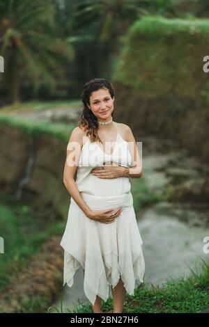 Jeune femme enceinte en robe blanche avec vue sur les rizières en terrasses de Bali dans la lumière du soleil du matin. Harmonie avec la nature. Concept de la grossesse. Banque D'Images