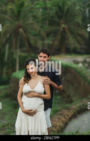 Jeune femme enceinte latine avec mari avec la vue étonnante de Ubud rizières en terrasses. Pregnant couple heureux ensemble. Banque D'Images