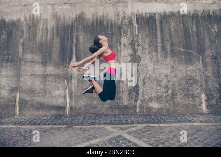 Bravo ! Sport de fitness femme dans la mode sportswear est de sauter dans la rue de la ville sur fond gris béton. Vêtements et chaussures de sport pour l'extérieur Banque D'Images