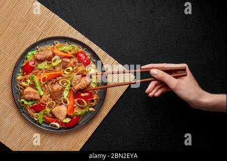 PAD Woon Sen ou Thai Pork Glass Noodle Stir-Fry dans une assiette noire sur fond d'ardoise sombre. PAD Woon Sen est un plat de cuisine thaï composé de nouilles de haricots en verre, de viande Banque D'Images