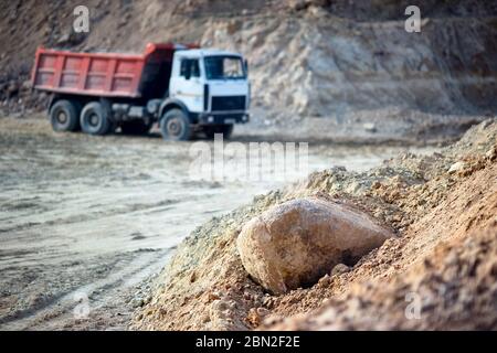 Pile de roches de minerai sur fond défocaé avec un lourd camion d'extraction minière de plusieurs tonnes exportant des minéraux de la mine à ciel ouvert. Concept de l'expédition, et Banque D'Images