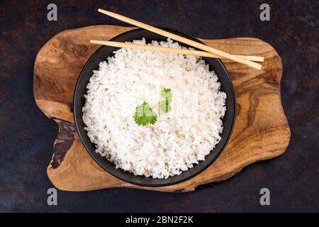 Riz blanc sur une assiette noire avec baguettes sur une table en bois. Banque D'Images