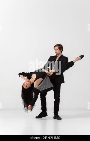 Jeunes danseurs de ballet gracieux dans un style noir minimaliste isolé sur fond blanc de studio. Art, mouvement, action, flexibilité, inspiration concept. Danseurs de ballet caucasiens flexibles, sauts sans poids. Banque D'Images