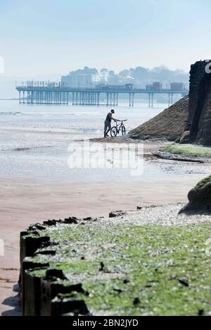 Un homme pousse son vélo près de la jetée fermée sur la plage de Paignton pendant le verrouillage du coronavirus, au Royaume-Uni Banque D'Images