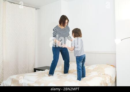 Jeune mère heureuse s'amuser avec sa petite fille mignonne, sauter sur un lit dans la chambre, jouer et rire, jeux actifs à la maison, corps entier même c Banque D'Images