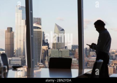 Homme d'affaires silhouette utilisant un smartphone à la fenêtre urbaine Banque D'Images