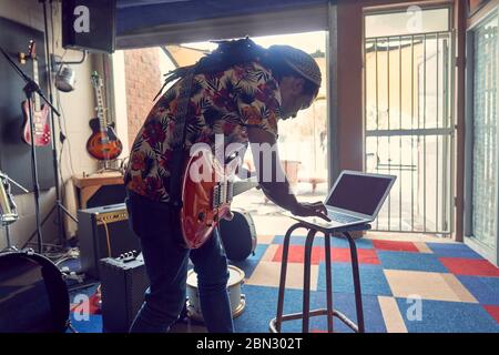 Musicien de sexe masculin avec ordinateur portable et guitare électrique dans un studio d'enregistrement en garage Banque D'Images