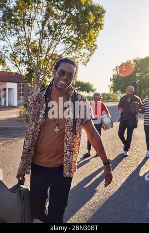 Portrait heureux musicien masculin portant une sacoche de guitare dans une rue ensoleillée Banque D'Images