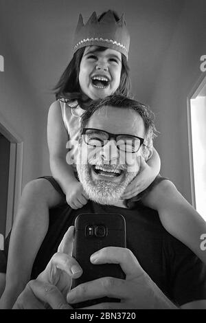 Selfie d'un père souriant portant sa fille sur les épaules devant un miroir. Banque D'Images