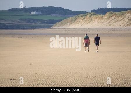 Isolement sur la plage vide et déserte de Newborough. Père et fils marchent ensemble pour faire de l'exercice quotidien sur la plage isolée du Royaume-Uni. Vacances d'été Royaume-Uni. Banque D'Images