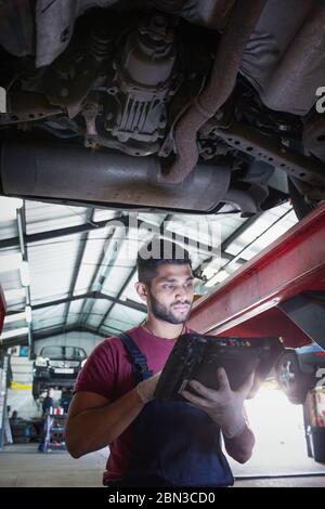 Mécanicien de sexe masculin utilisant un équipement de diagnostic sous une voiture dans un atelier de réparation automobile Banque D'Images