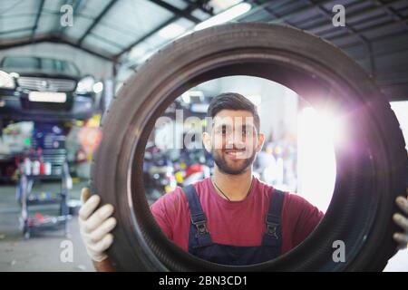 Portrait homme confiant, souriant mécanicien tenant le pneu dans l'atelier de réparation automobile Banque D'Images