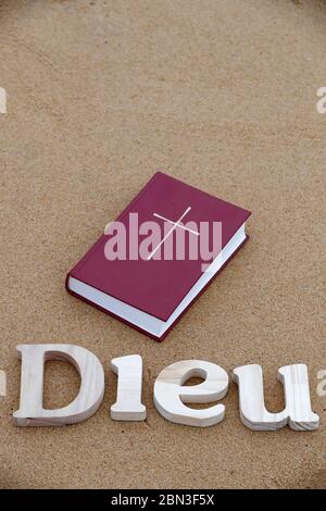 Lettres en bois formant le mot Dieu avec la Bible sur fond de sable de plage. Symbole chrétien. Banque D'Images