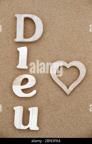Lettres en bois formant le mot Dieu ( dieu ) avec coeur sur fond de sable de plage. Symbole chrétien. Banque D'Images