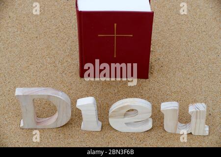 Lettres en bois formant le mot Dieu avec la Bible sur fond de sable de plage. Symbole chrétien. Banque D'Images