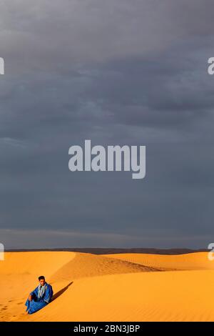 Jeune marocain assis sur une dune de sable au Sahara, Maroc. Banque D'Images