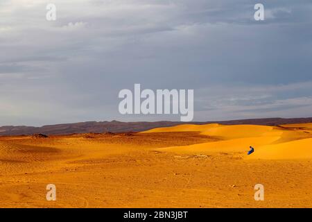 Jeune marocain assis sur une dune de sable au Sahara, Maroc. Banque D'Images