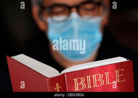 Homme lisant la bible avec un masque jetable pour éviter le coronavirus contagieux ( COVID-19). France. Banque D'Images