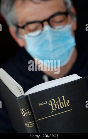 Homme lisant la bible avec un masque jetable pour éviter le coronavirus contagieux ( COVID-19). France. Banque D'Images