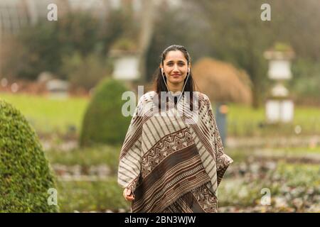 Photo moyenne d'une jolie femme indienne portant un poncho souriant dans un jardin topiaire ornemental. Banque D'Images