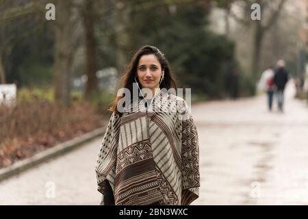 Beauté indienne portant poncho et écoutant les écouteurs posé sur la route du parc. Banque D'Images