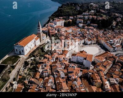 Vue aérienne sur la ville de Piran avec la place principale de Tartini, les bâtiments anciens avec des toits rouges, l'église paroissiale de Saint-Georges et la mer Adriatique en Slovénie Banque D'Images