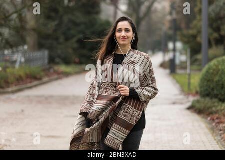 Belle femme portant un poncho et écoutant des écouteurs souriant pour l'appareil photo à l'extérieur. Banque D'Images
