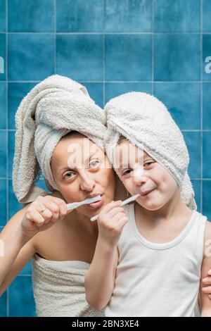 Une femme et un garçon avec des serviettes sur la tête se brossant les dents. Banque D'Images