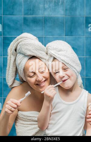 Une femme et un garçon avec des serviettes sur la tête se brossant les dents. Banque D'Images