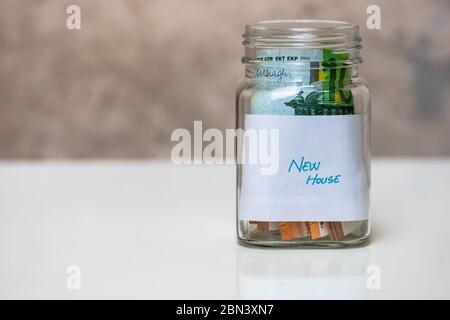 Composition avec des billets d'argent d'économie dans un pot en verre avec texte nouvelle maison. Concept d'investissement et de maintien de l'argent, isolé. Banque D'Images