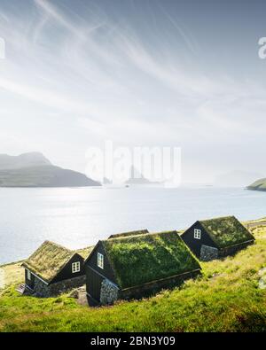 Vue pittoresque sur les maisons couvertes d'herbe de faroese, dans le village de Bour. Drangarnir et Tindholmur des piles de mer en arrière-plan. Île De Vagar, Îles Féroé, Danemark. Photographie de paysage Banque D'Images