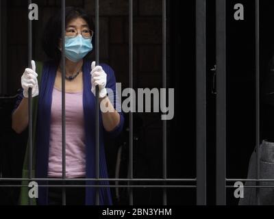 Femme asiatique avec masque et gants derrière une grille de barres - grille - pendant le confinement du coronavirus de confinement de la maladie COVID-19. Banque D'Images