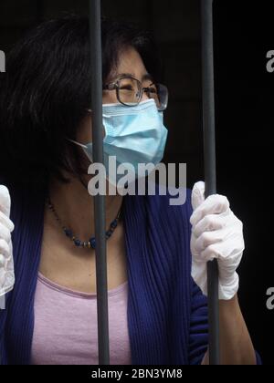 Femme asiatique avec masque et gants derrière une grille de barres - grille - pendant le confinement du coronavirus de confinement de la maladie COVID-19. Banque D'Images