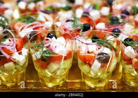 Salade de tomates, concombres, oignons, olives et persil, en verres debout sur une table dorée Banque D'Images